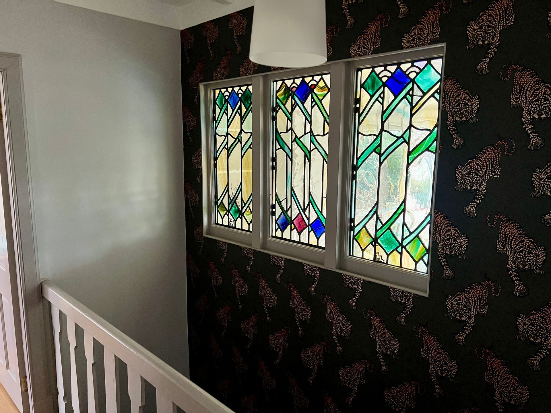 Stair landing with stained-glass windows and dark floral wallpaper beside a white railing