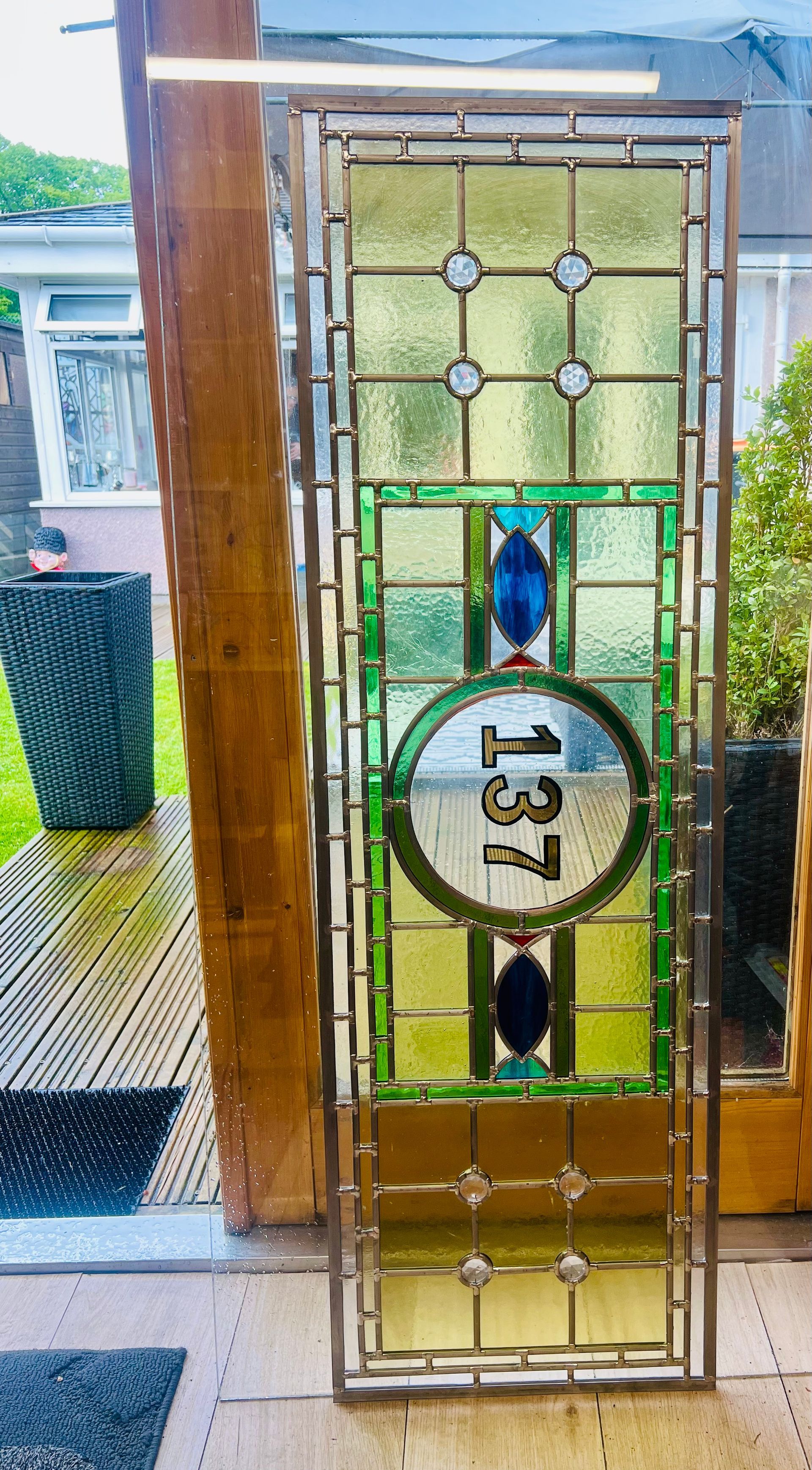 Decorative stained-glass front door with gold frame and circular house number 13, seen from outside.