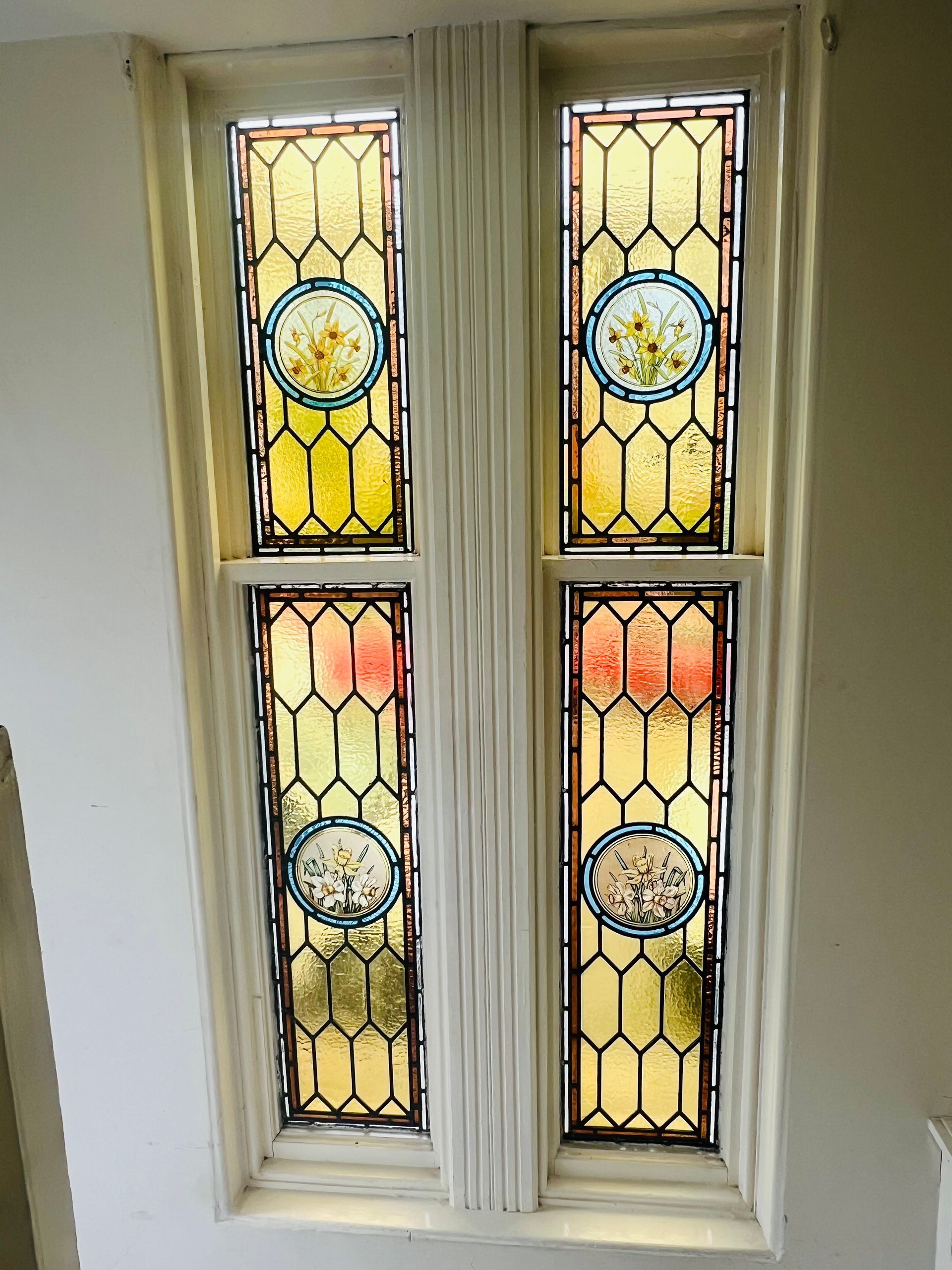 Four stained-glass window panels in a white wall, with yellow and orange glass accents.