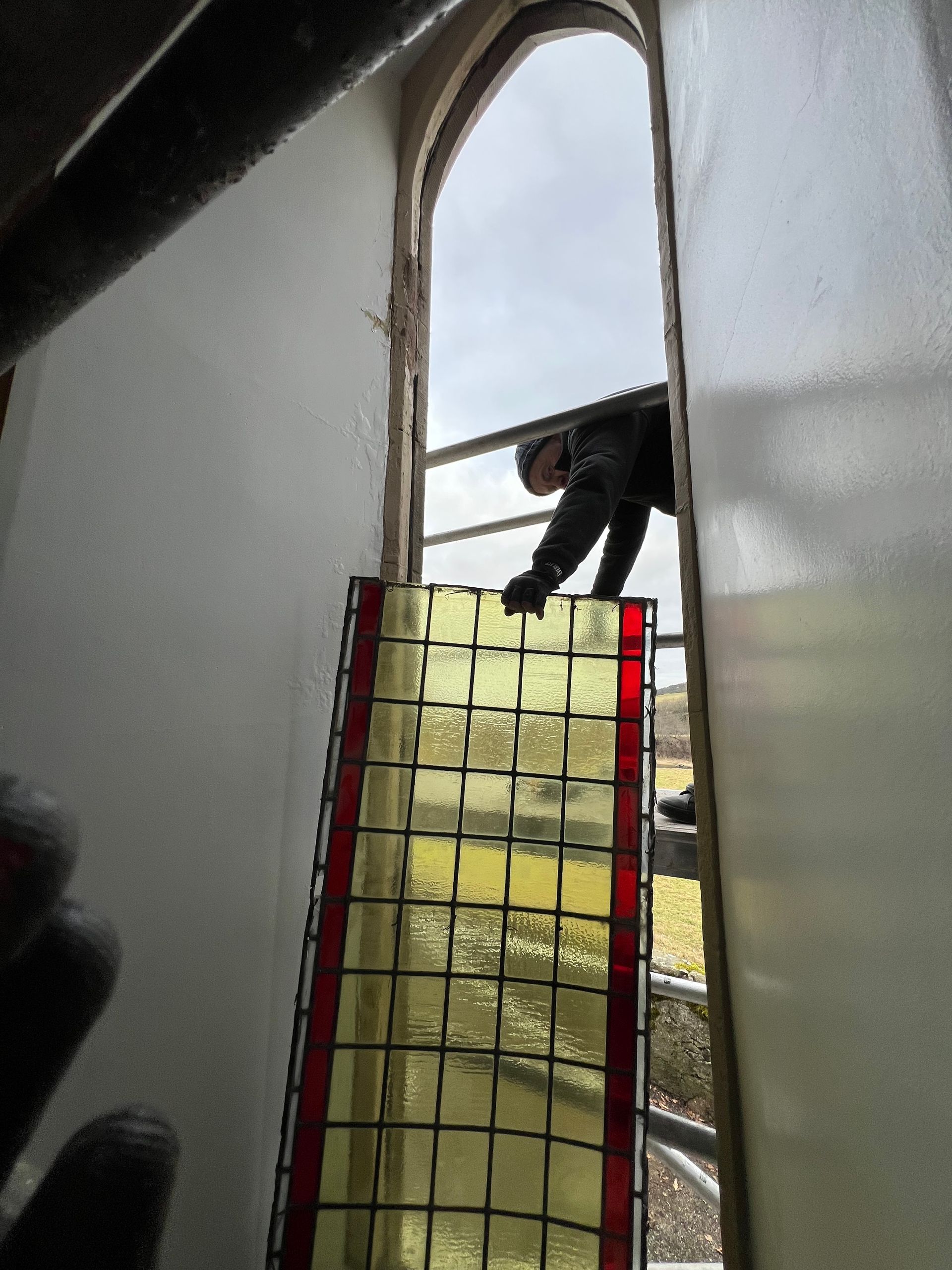 Person leaning through a narrow open window above a red net barrier on a stairwell.