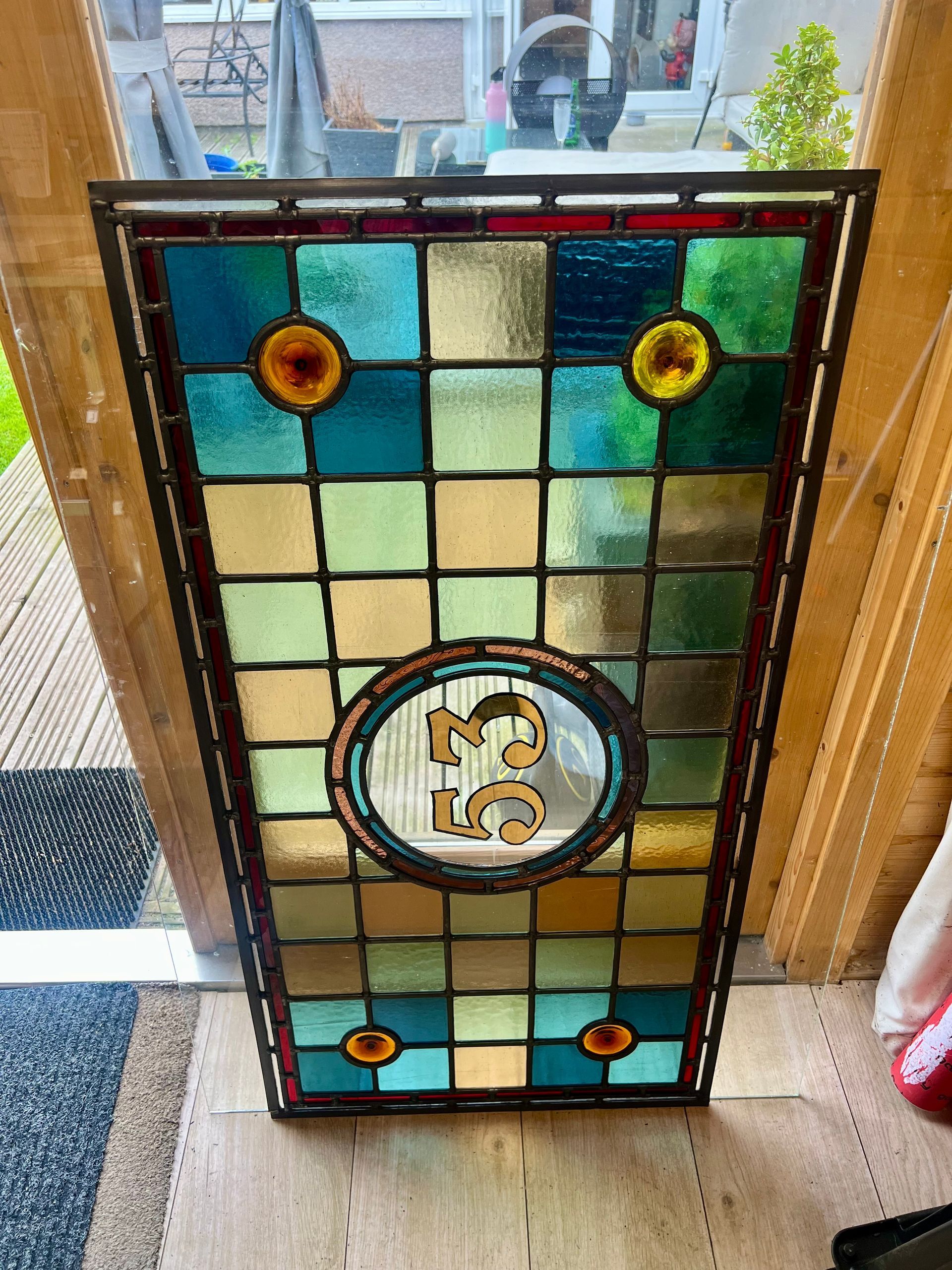 Stained glass panel with teal, cream, and amber squares in a wooden frame by a window