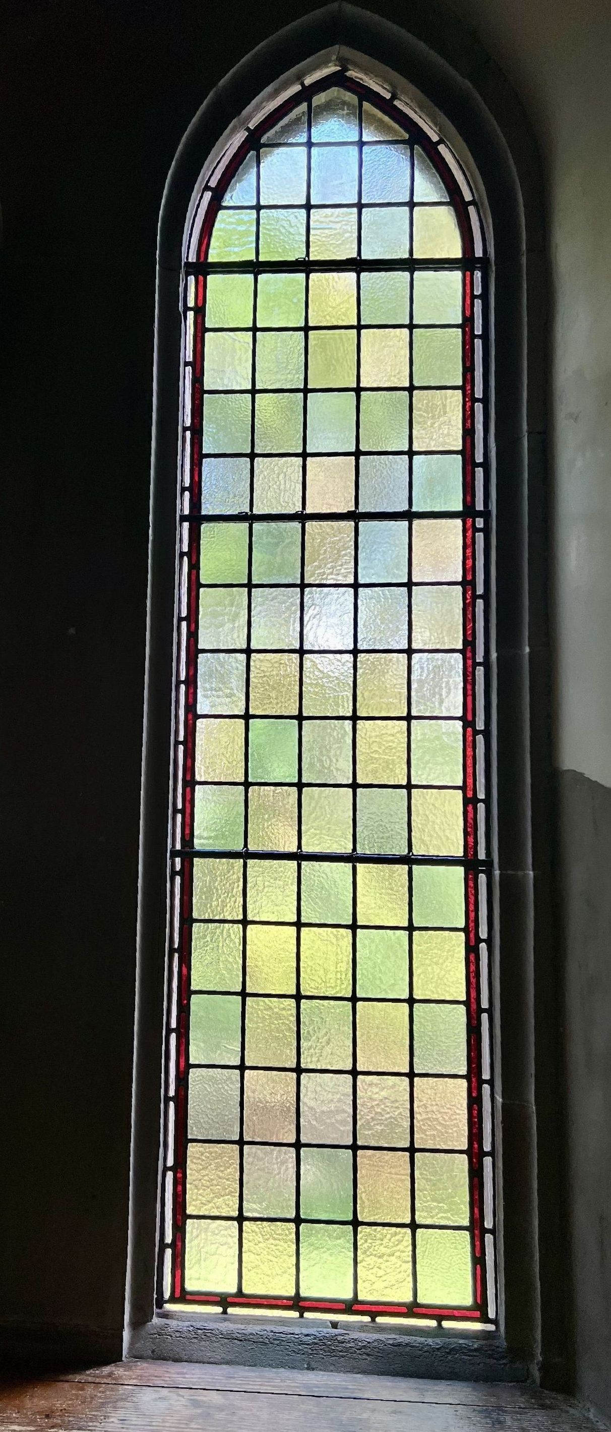 Tall arched stained-glass window with a black frame and colorful panes in a dim interior