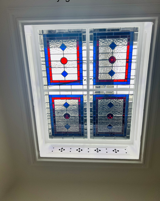 Four-panel stained glass window with blue and red geometric patterns in a white frame