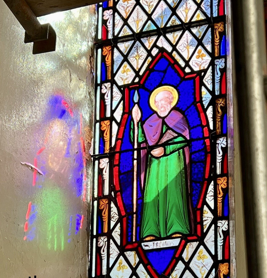 Stained glass panel of a haloed figure in a purple robe and green cloak beside frosted glass.