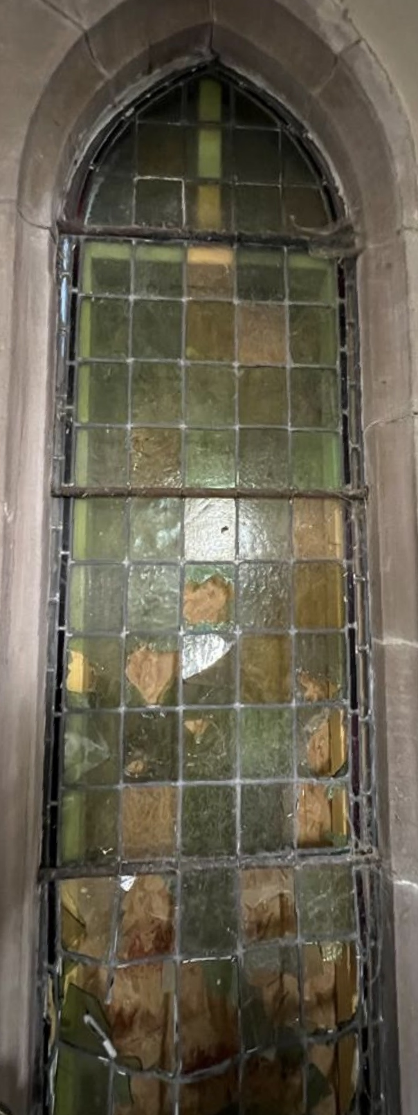 Tall arched stained-glass window with green, amber, and clear panes in a stone wall