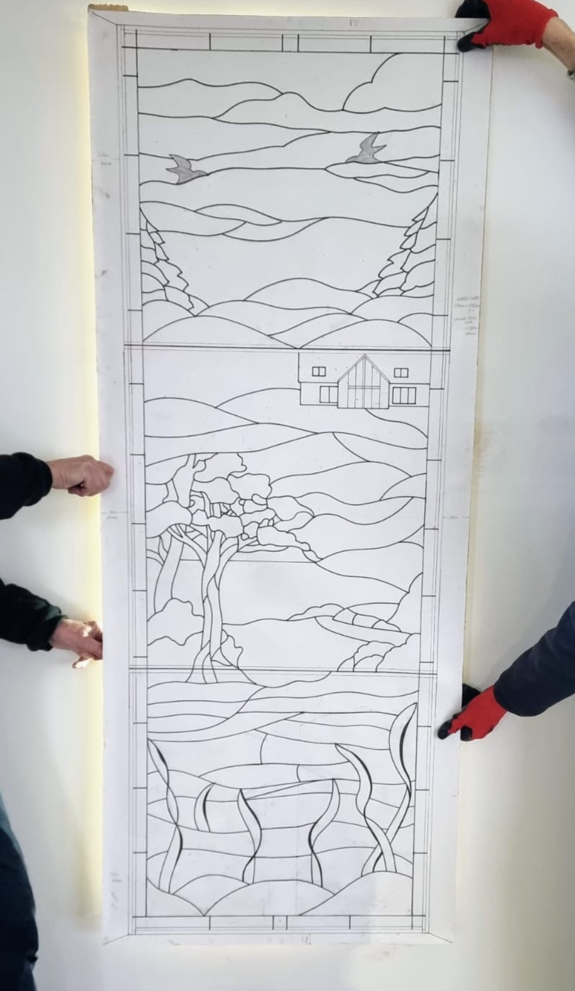 Four people hold a tall paper mural outline showing landscapes and buildings.
