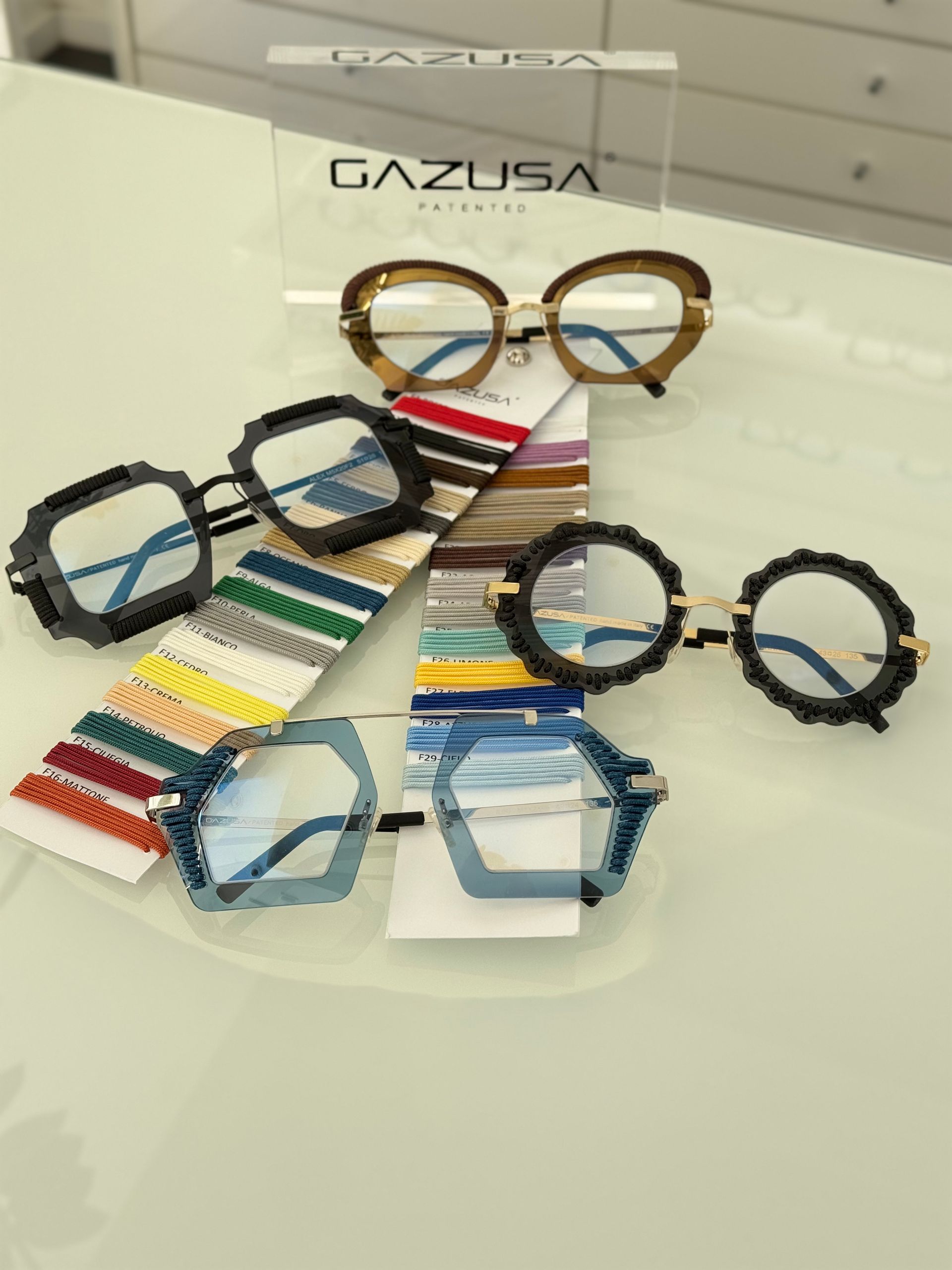 Esposizione di occhiali: cinque paia con montature, colori e design unici, insieme a campioni di colore e un cartello 