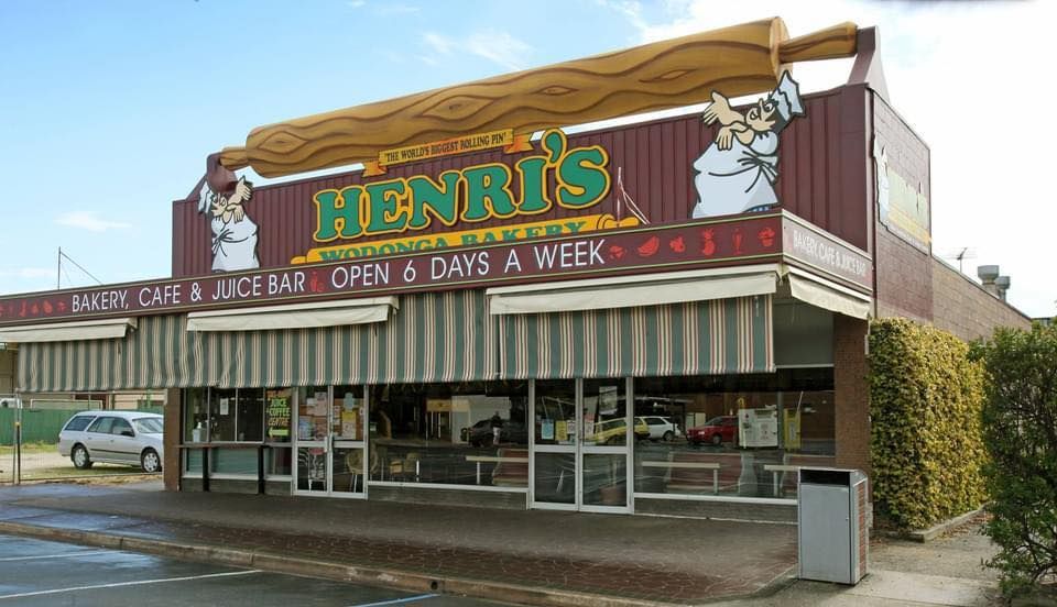 Henri's Bakery Cafe with awning, sign of a chef, and large bread sculpture on roof. Open 6 days a week.