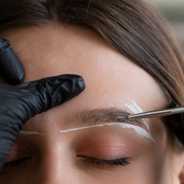 A woman is getting her eyebrows painted by a person wearing black gloves.