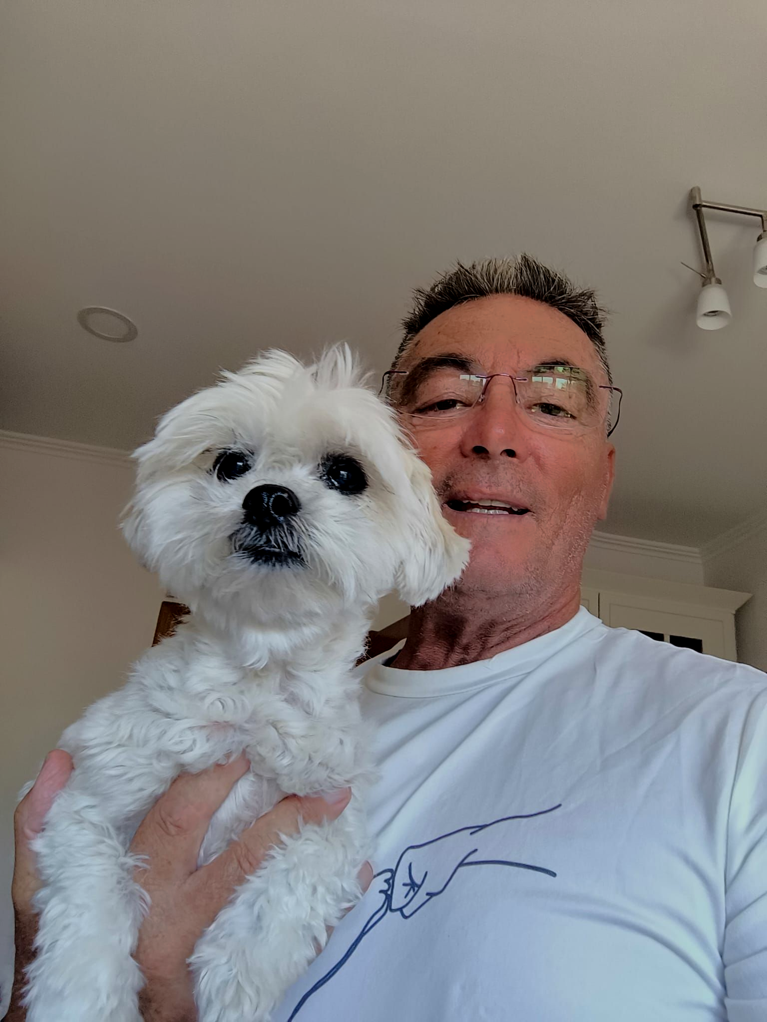 Man holding a small white dog indoors, both facing the camera.