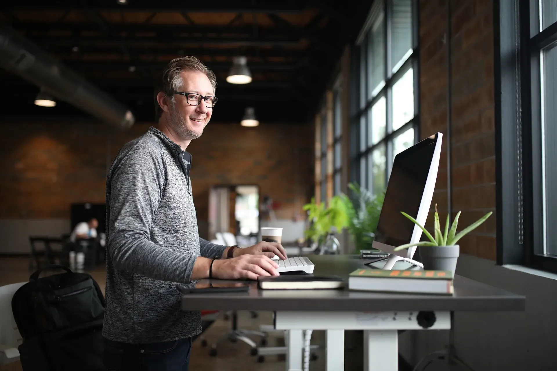 A man is standing at a standing desk in front of a computer.