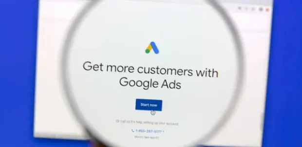A person is holding a magnifying glass in front of a screen that says `` get more customers with google ads ''.