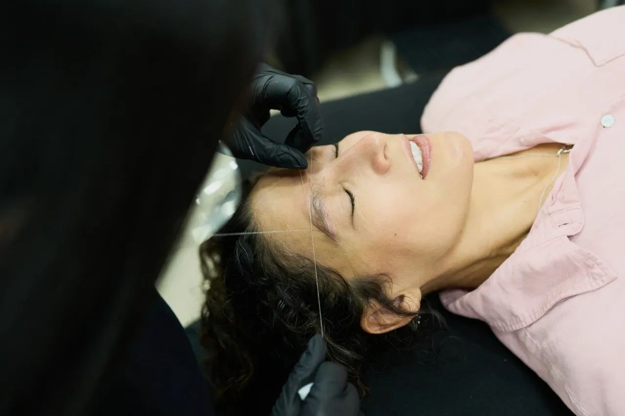 Person lying back in a salon chair with eyes closed, wearing a pink shirt and foil in their hair.