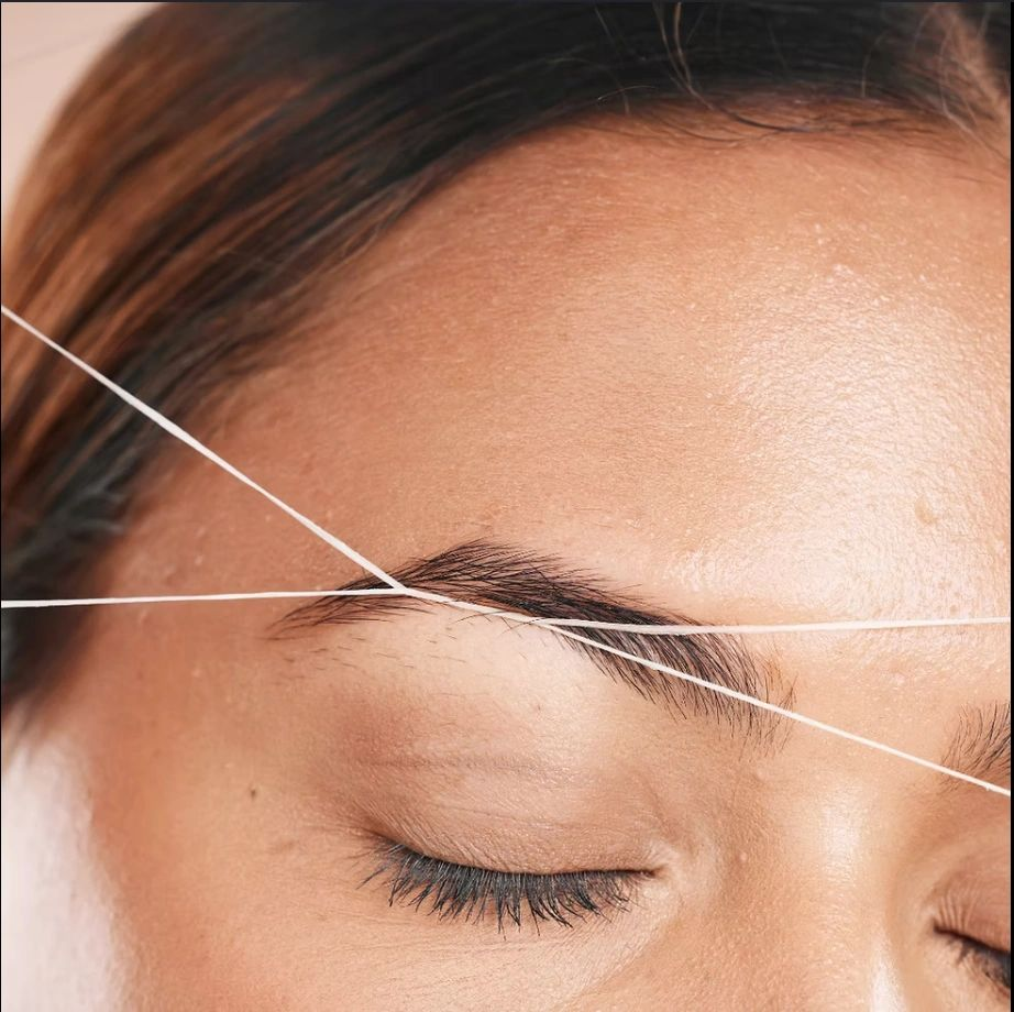 Woman’s closed eye during eyebrow threading, with thread stretched across the brow