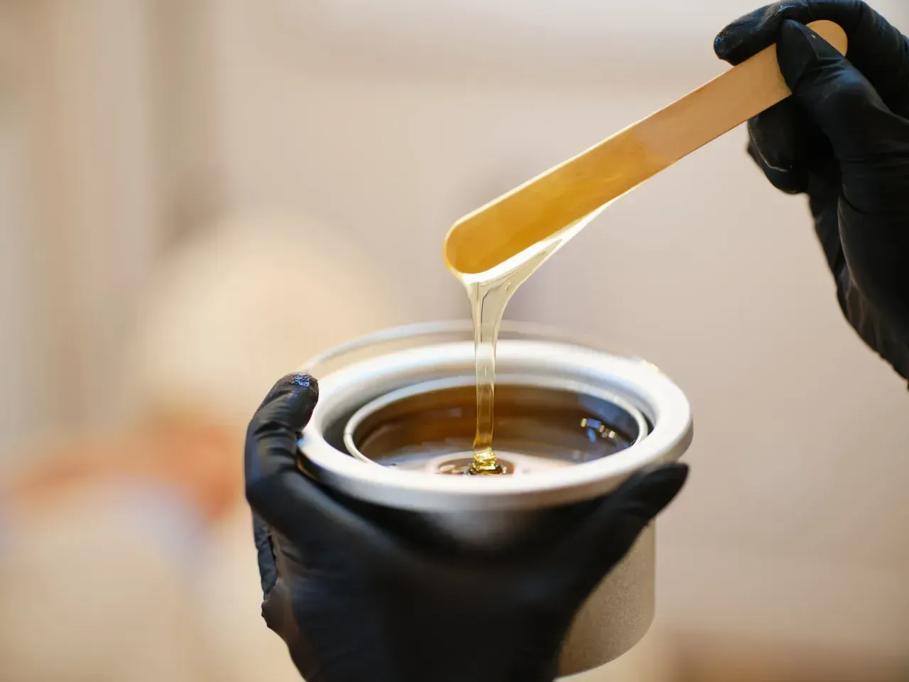Gloved hands holding a jar while a spatula drips amber wax or honey into it