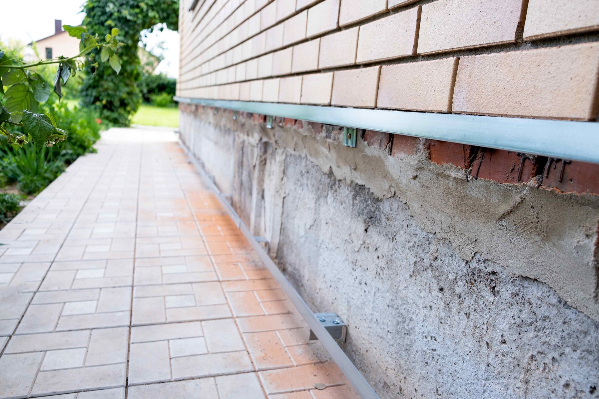Brick building wall with visible foundation; light-colored tiled walkway. Brick building wall with visible foundation; light-colored tiled walkway.