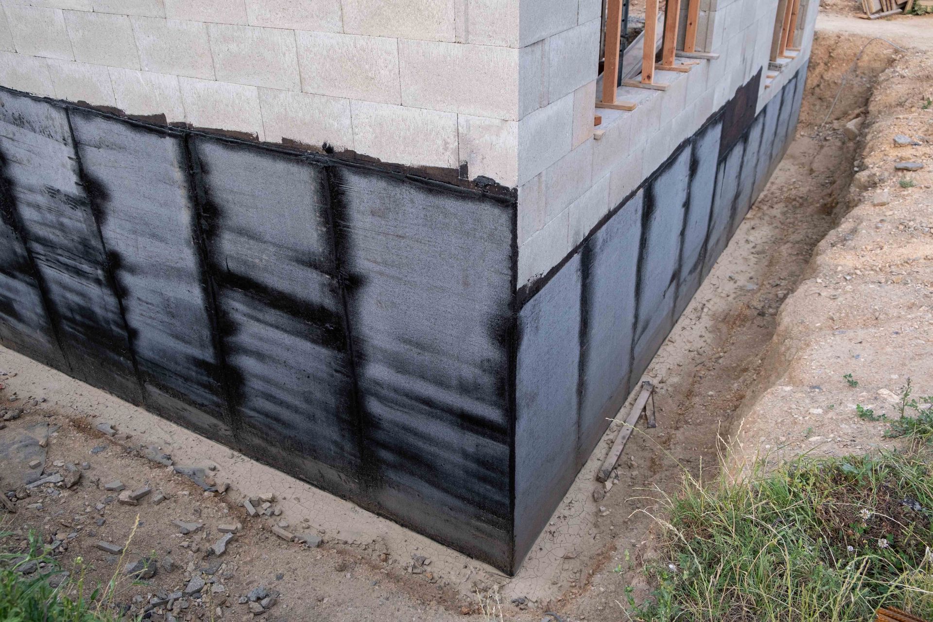 Foundation of a building with black waterproofing membrane applied, surrounded by excavated dirt. Foundation of a building with black waterproofing membrane applied, surrounded by excavated dirt.
