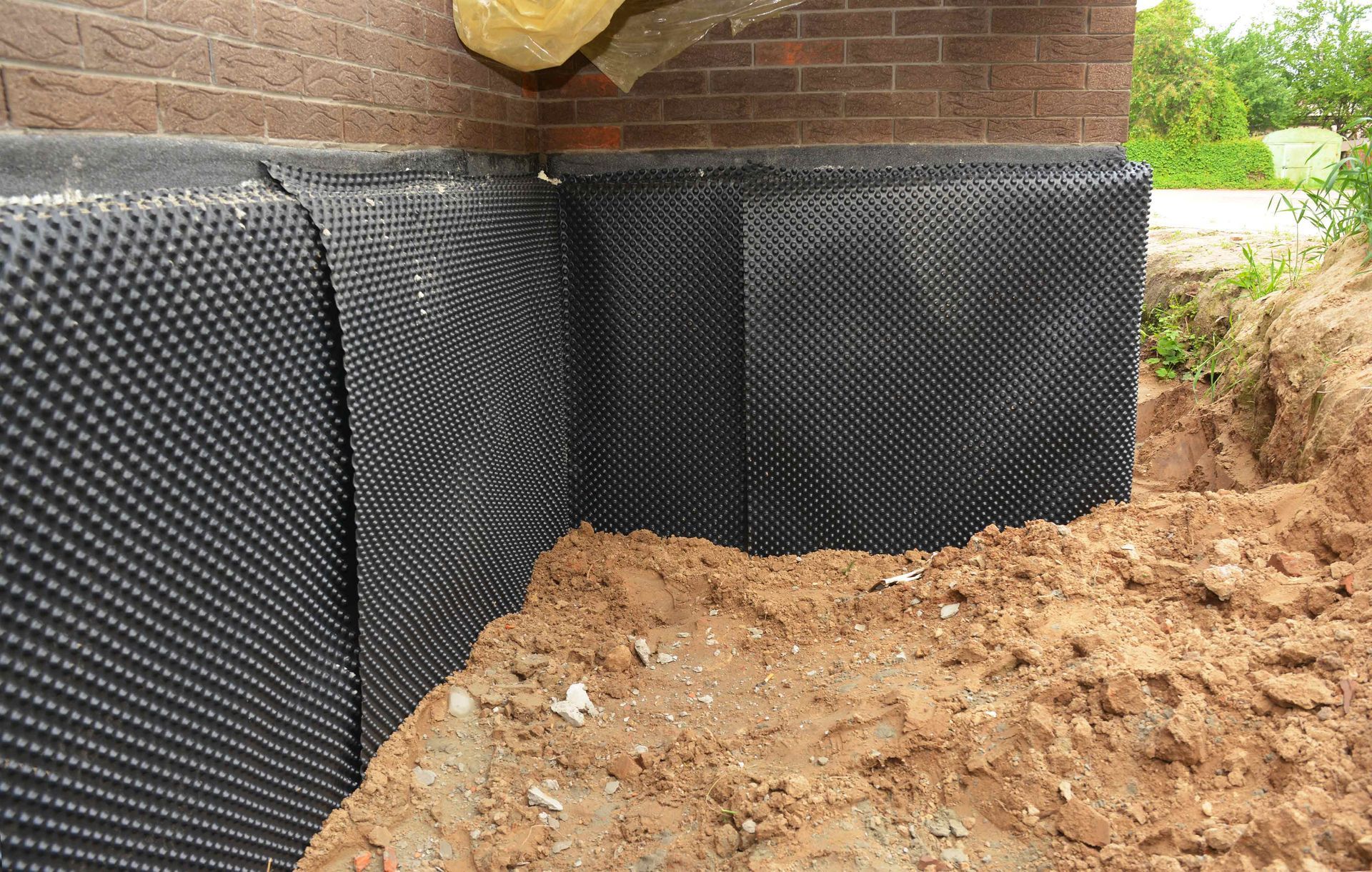 Black dimpled drainage membrane installed on a brick foundation wall with surrounding soil. Black dimpled drainage membrane installed on a brick foundation wall with surrounding soil.
