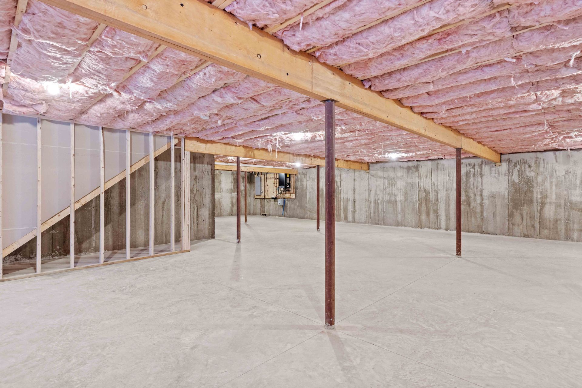 Unfinished basement with exposed ceiling insulation, wooden beams, concrete walls and floor, and support beams. Unfinished basement with exposed ceiling insulation, wooden beams, concrete walls and floor, and support beams.