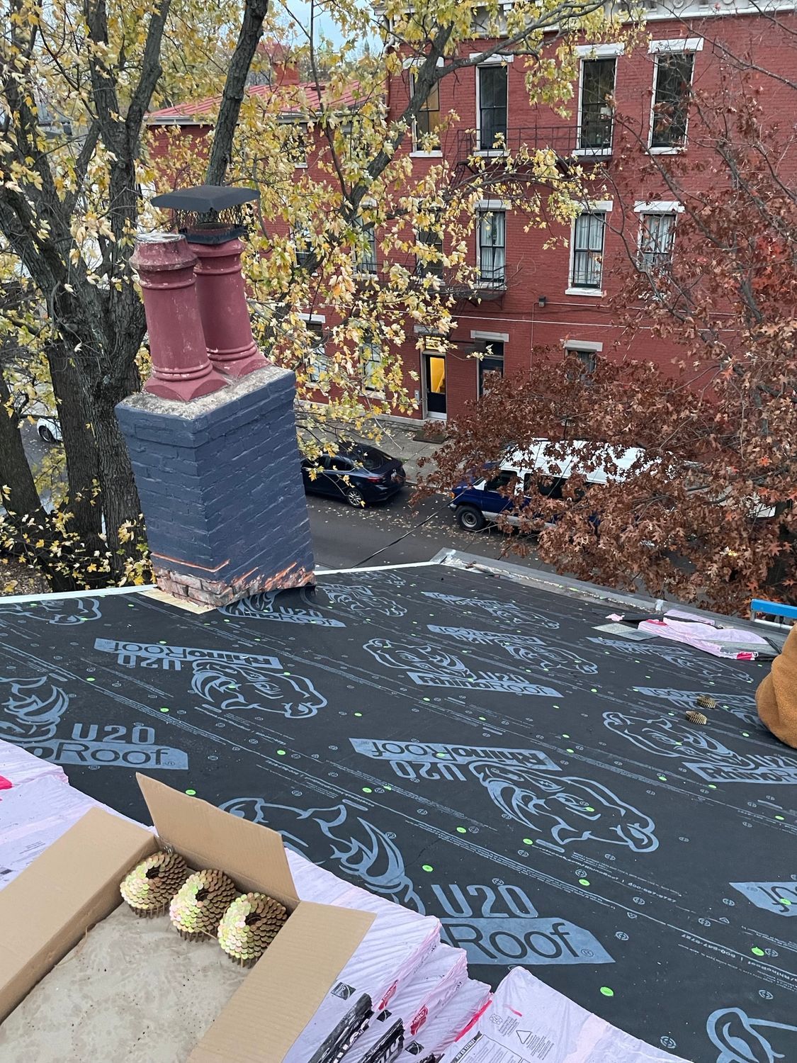 Rooftop view with a brick chimney, autumn trees, and red apartment building in the background.