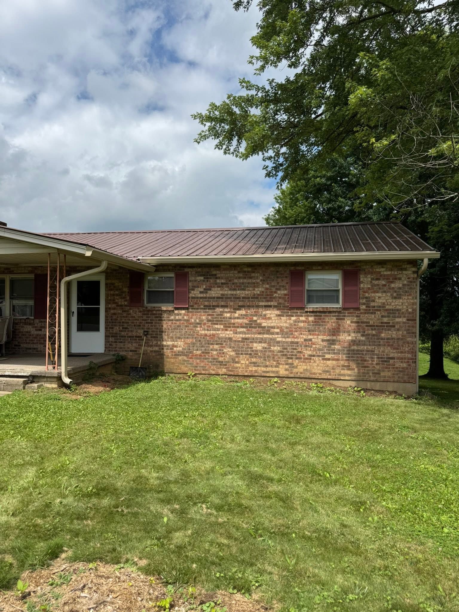 Single-story brick house with white door and windows, grassy front yard, and cloudy sky.