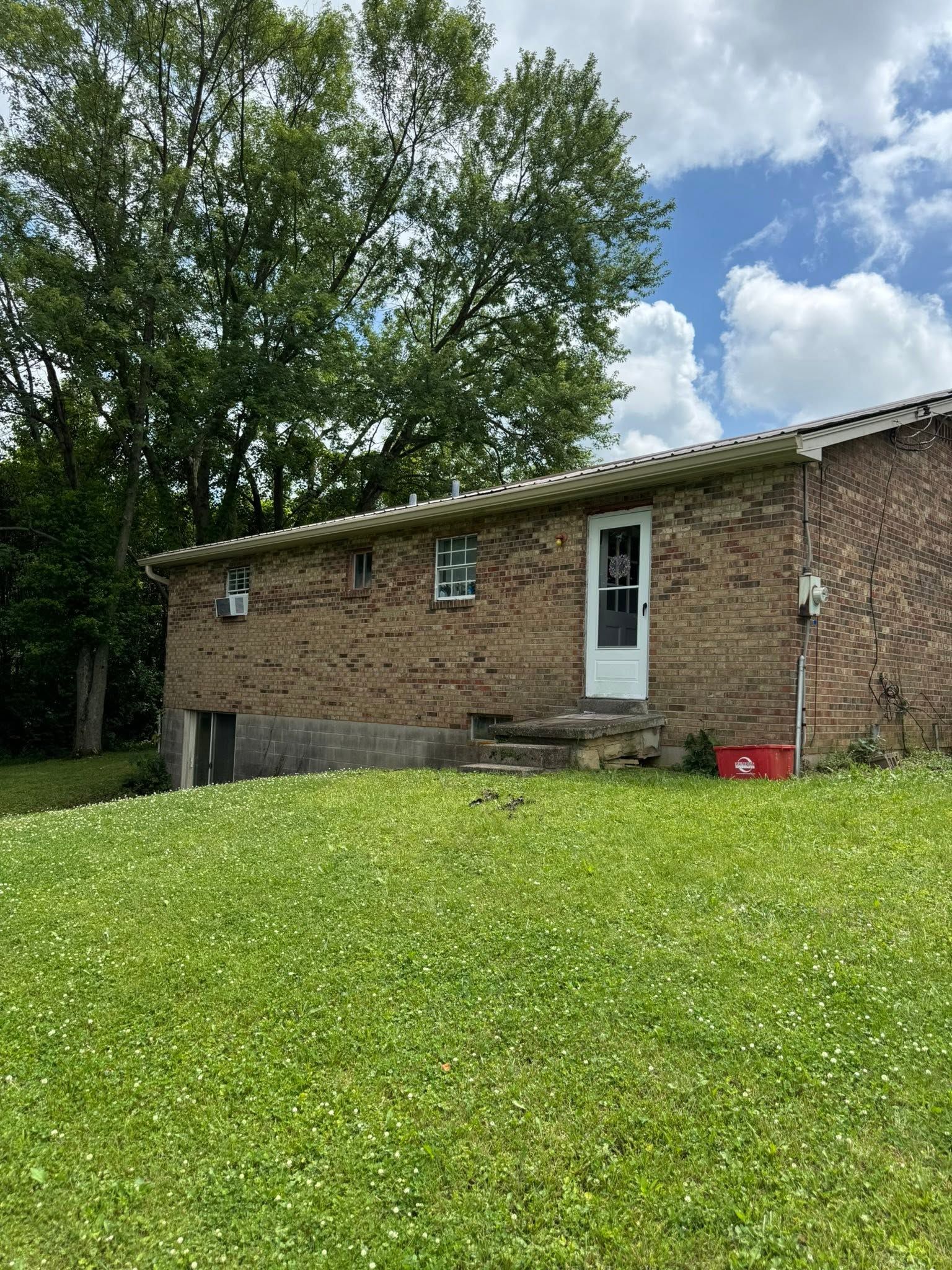 Brick house with seamless gutters beside trees under a partly cloudy sky