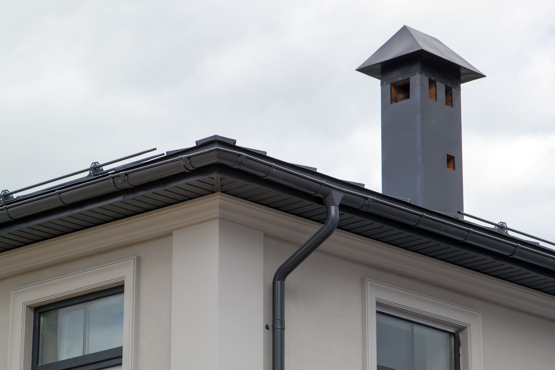 Roof Replacement Norwood, OH Rooftop chimney on a white house with a dark gray roof and cloudy sky above