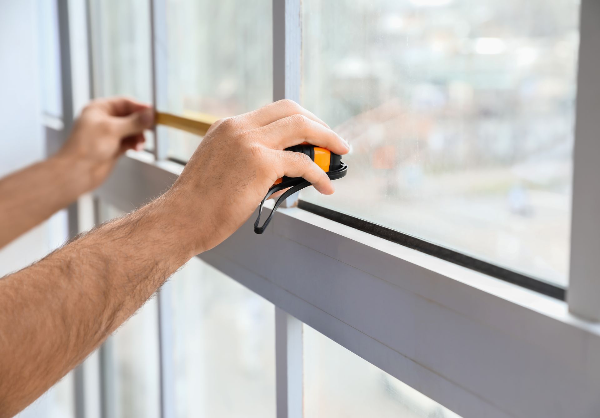 A contractor measuring a white window frame with a yellow tape measure before replacement