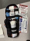 Open black trauma kit containing medical gauze and bandages, with NuStat and HyFin chest seals resting beside it.