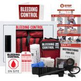 A Stop the Bleed kit featuring a wall cabinet, red supply pouches, a tourniquet, bandages, and an instruction card.