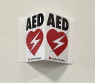 A white, V-shaped wall-mounted AED sign featuring red heart symbols with lightning bolts and the text 