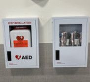 Two wall-mounted white cabinets; the left holds an AED, and the right holds emergency medical supplies.