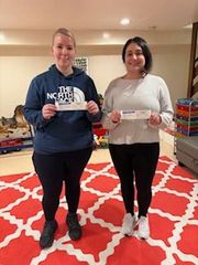 Two people stand in a room, holding small rectangular cards while smiling at the camera.