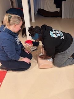 Two people practice CPR on a medical training mannequin on the floor.