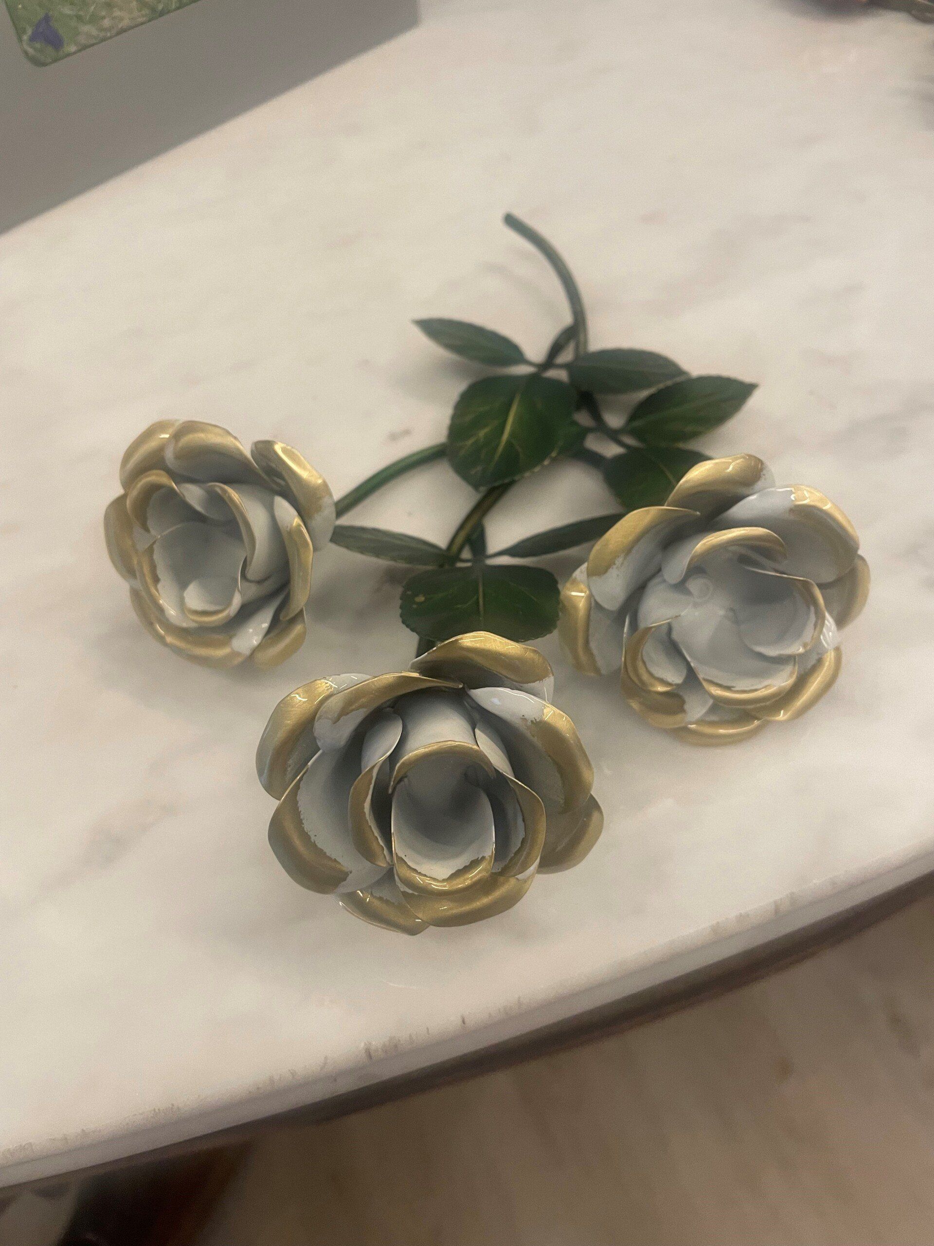 Tre rose bianche con finiture dorate e foglie verdi su una superficie di marmo.