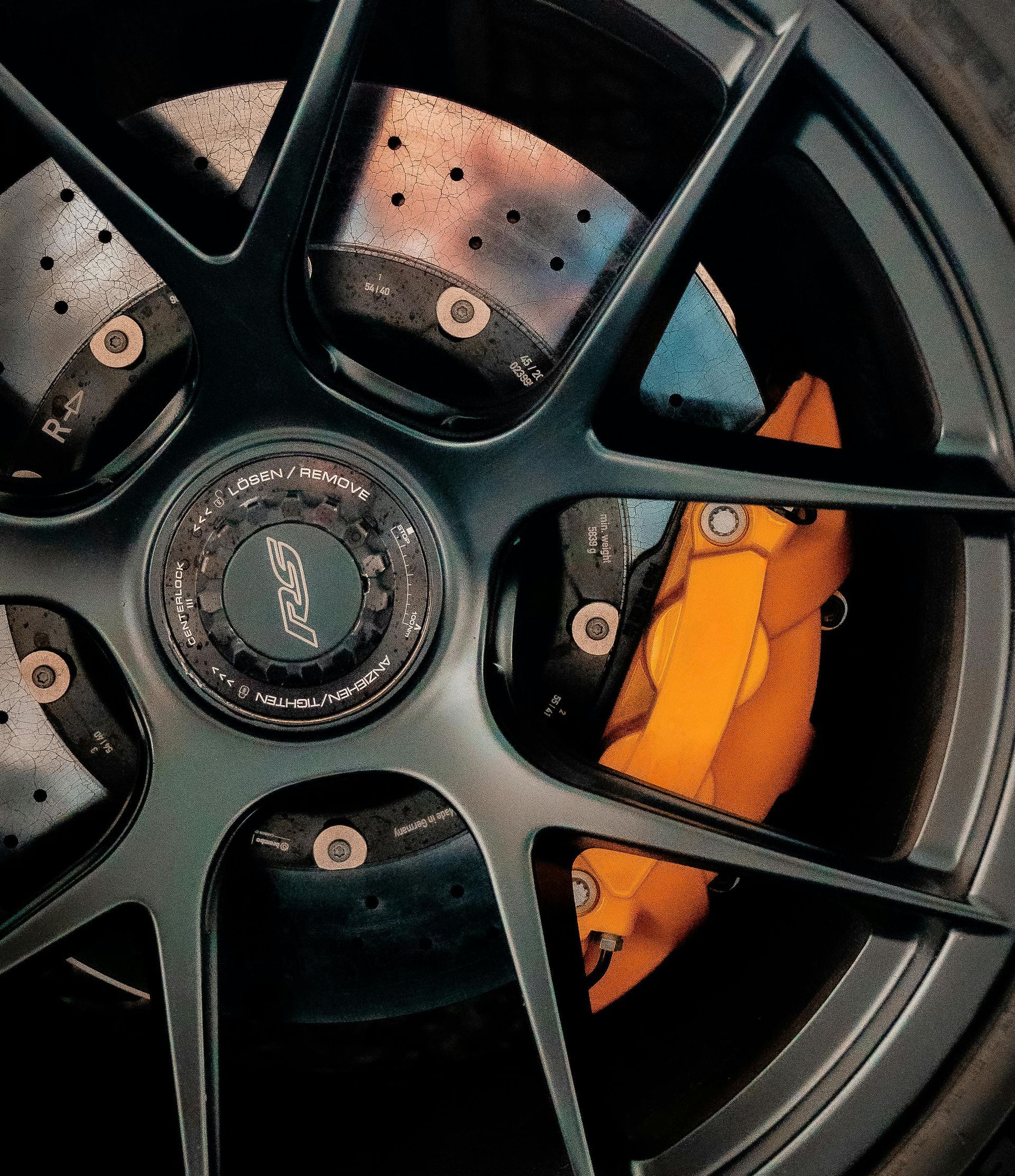 Close-up of a black alloy wheel with an orange brake caliper behind it.