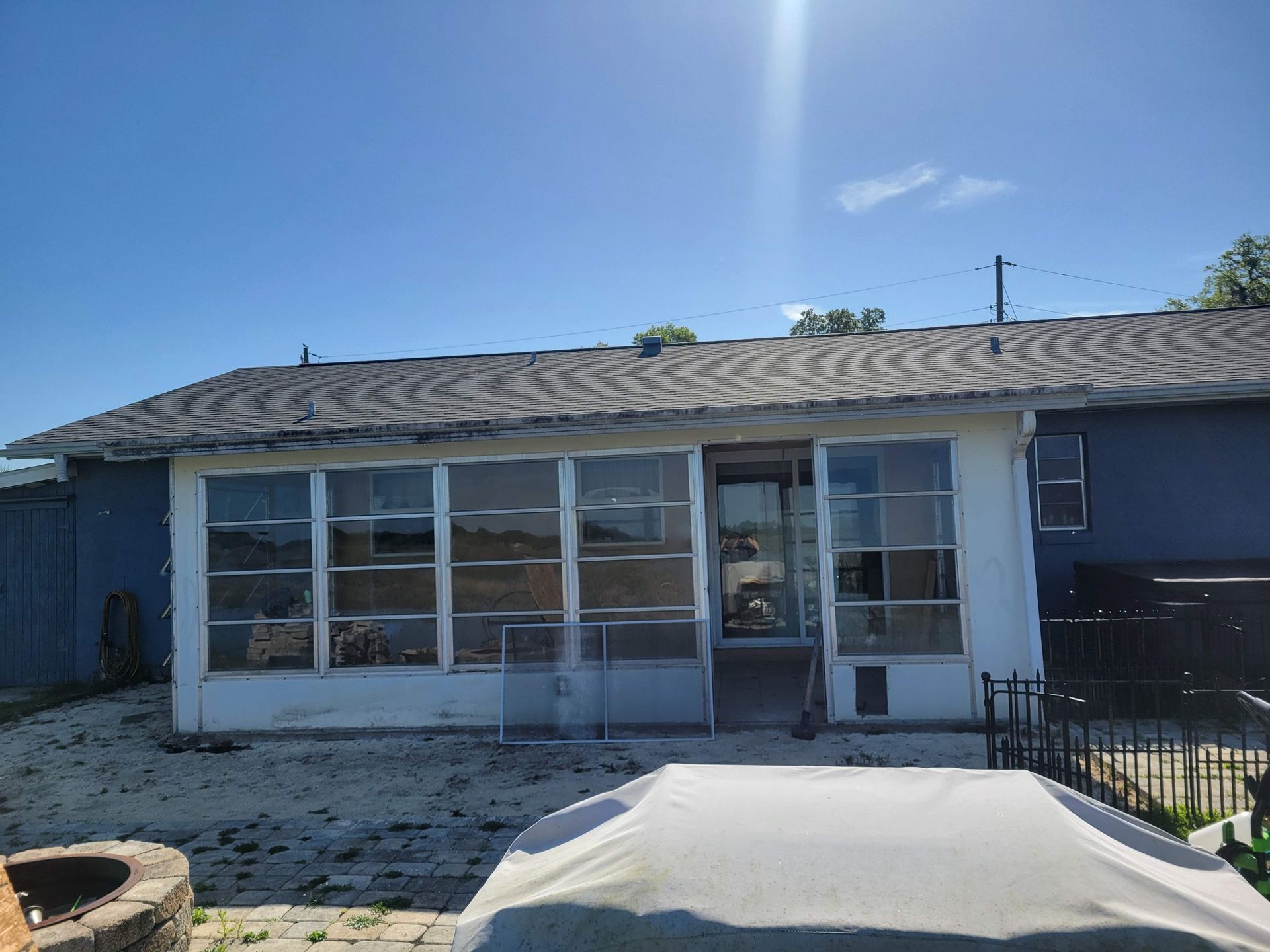 Blue house exterior with a sunroom and covered patio in bright sunlight