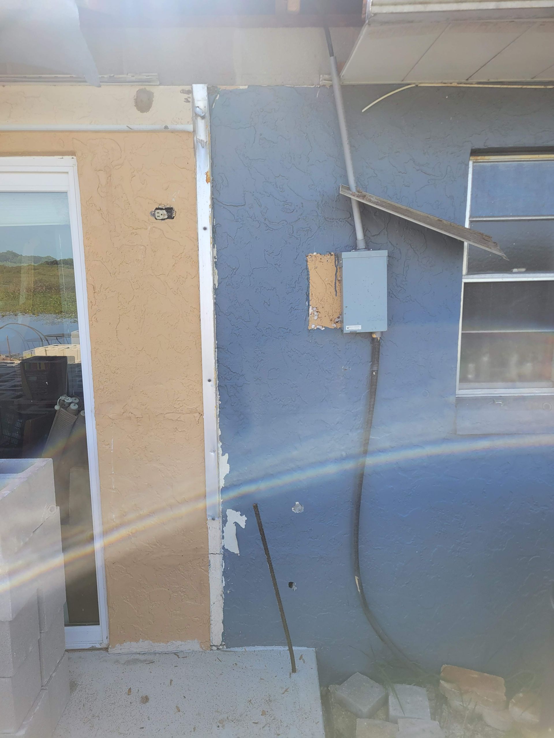 Exterior of a beige and blue building wall with a door, utility box, and pipes nearby