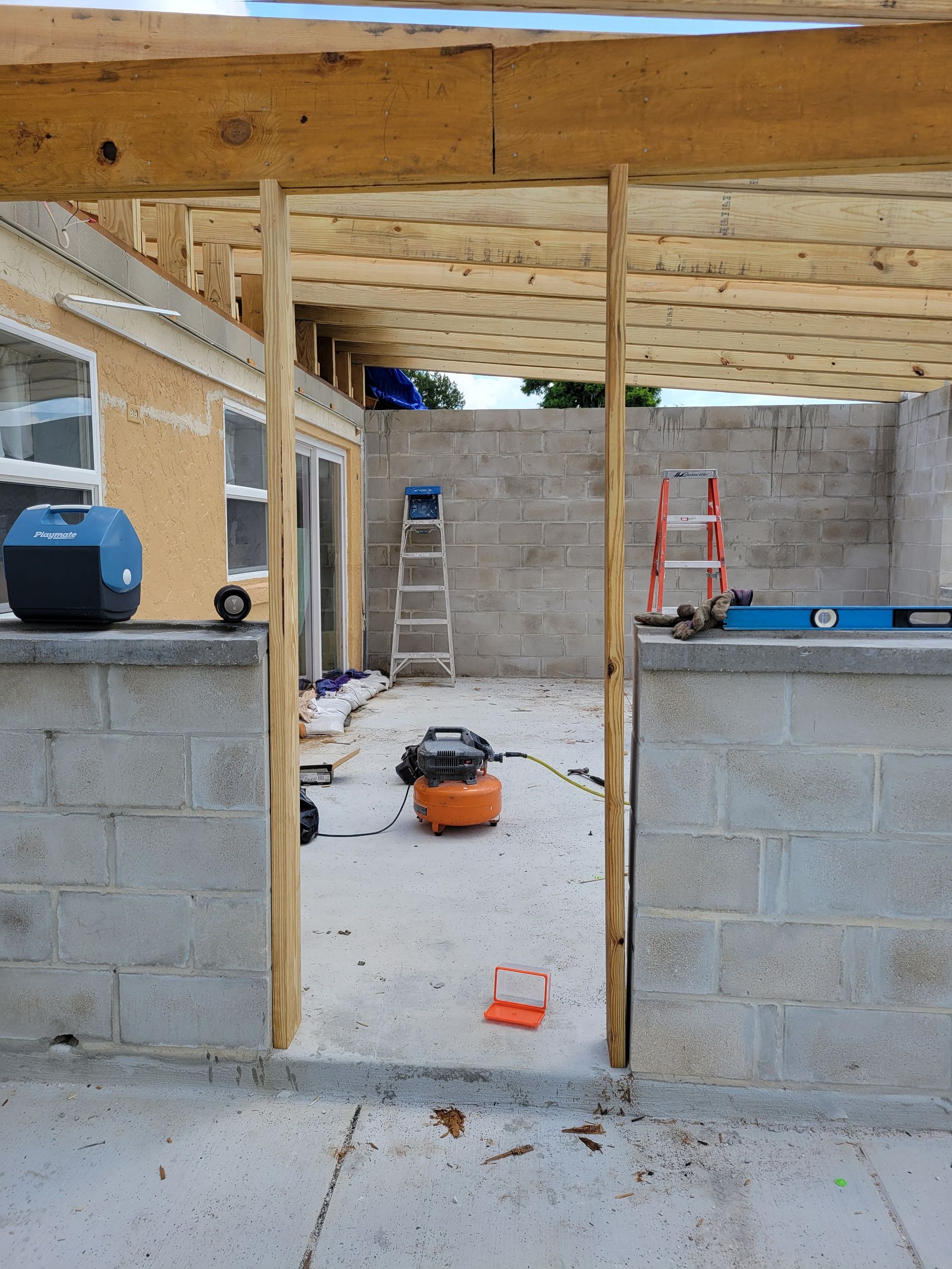 Partially built house interior with cinder block walls, exposed framing, tools, and a ladder outside the opening