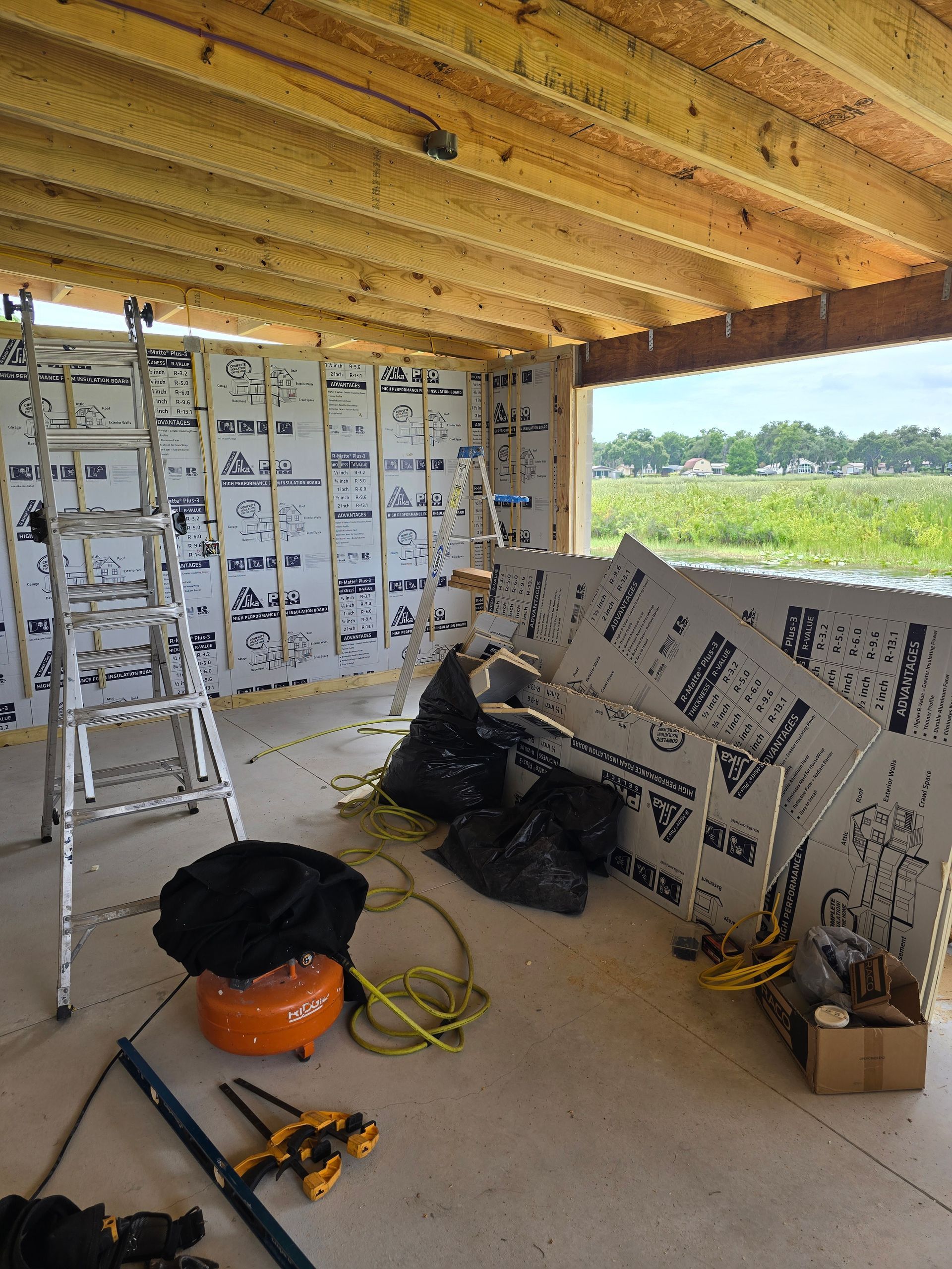 Partially finished porch with insulation boards, tools, ladder, and construction materials on the floor