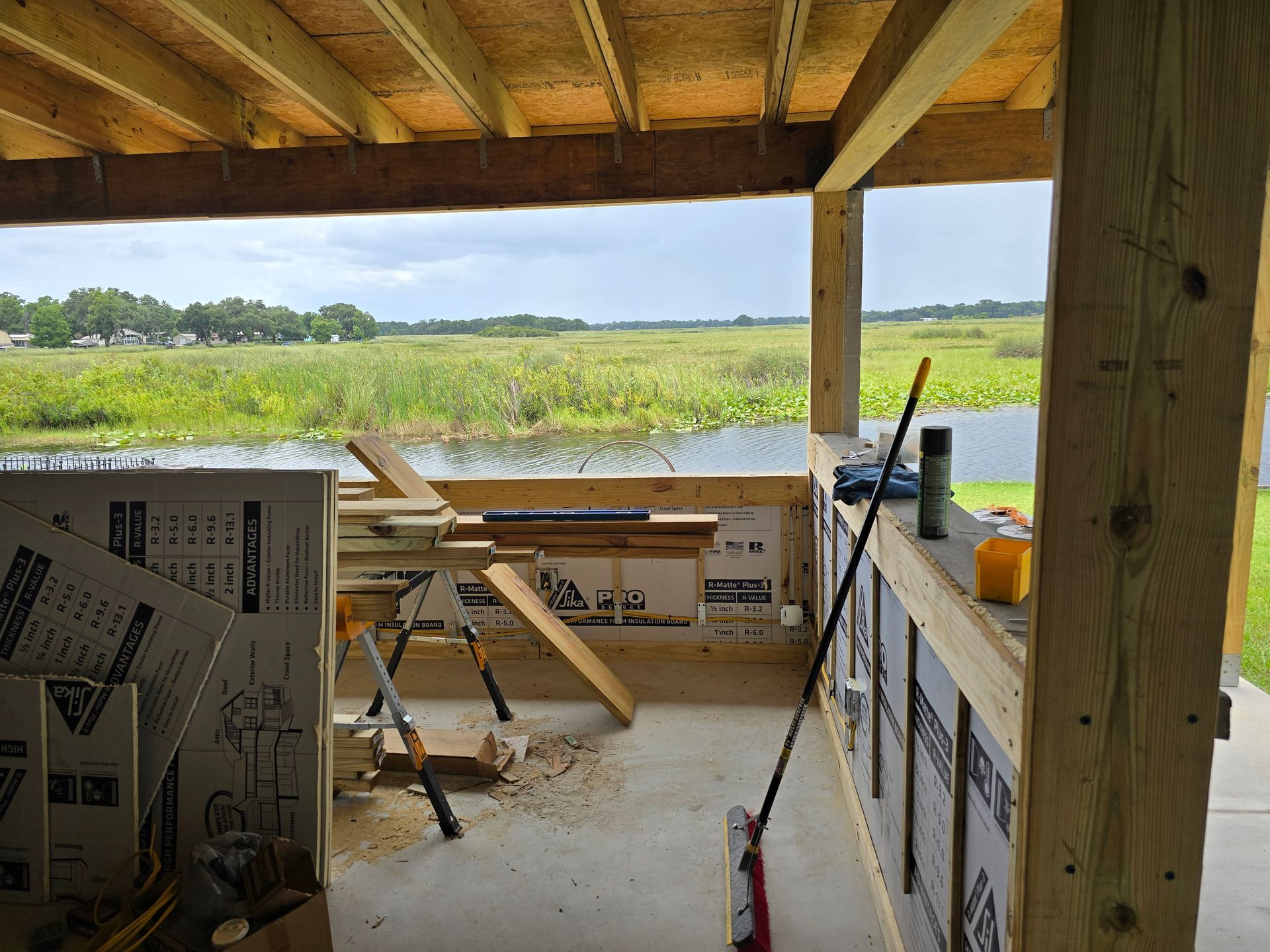 Wood-framed porch under construction with tools and materials, overlooking a green field.