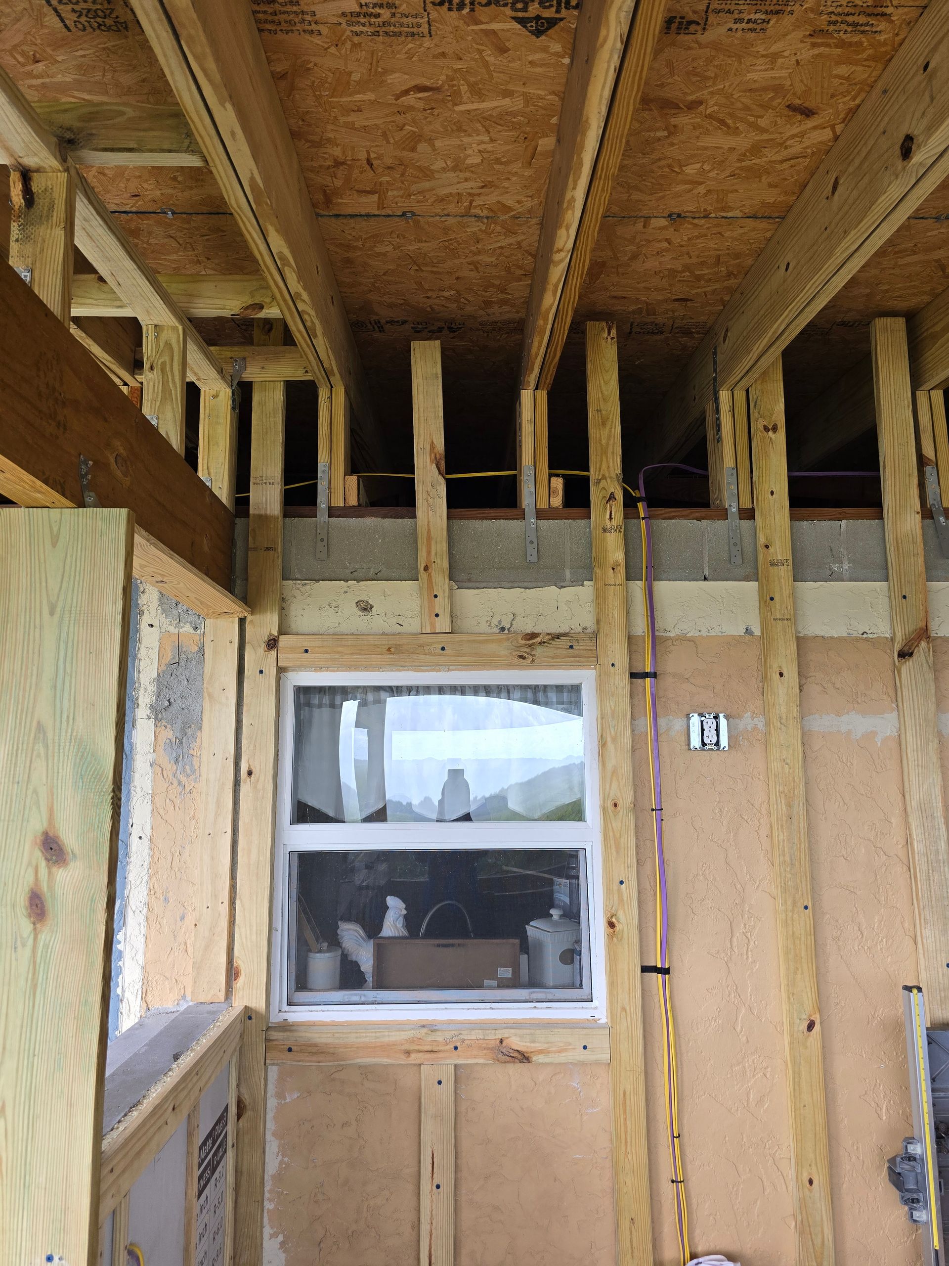 Partially finished room with exposed framing, plywood walls, a window, and insulation behind it