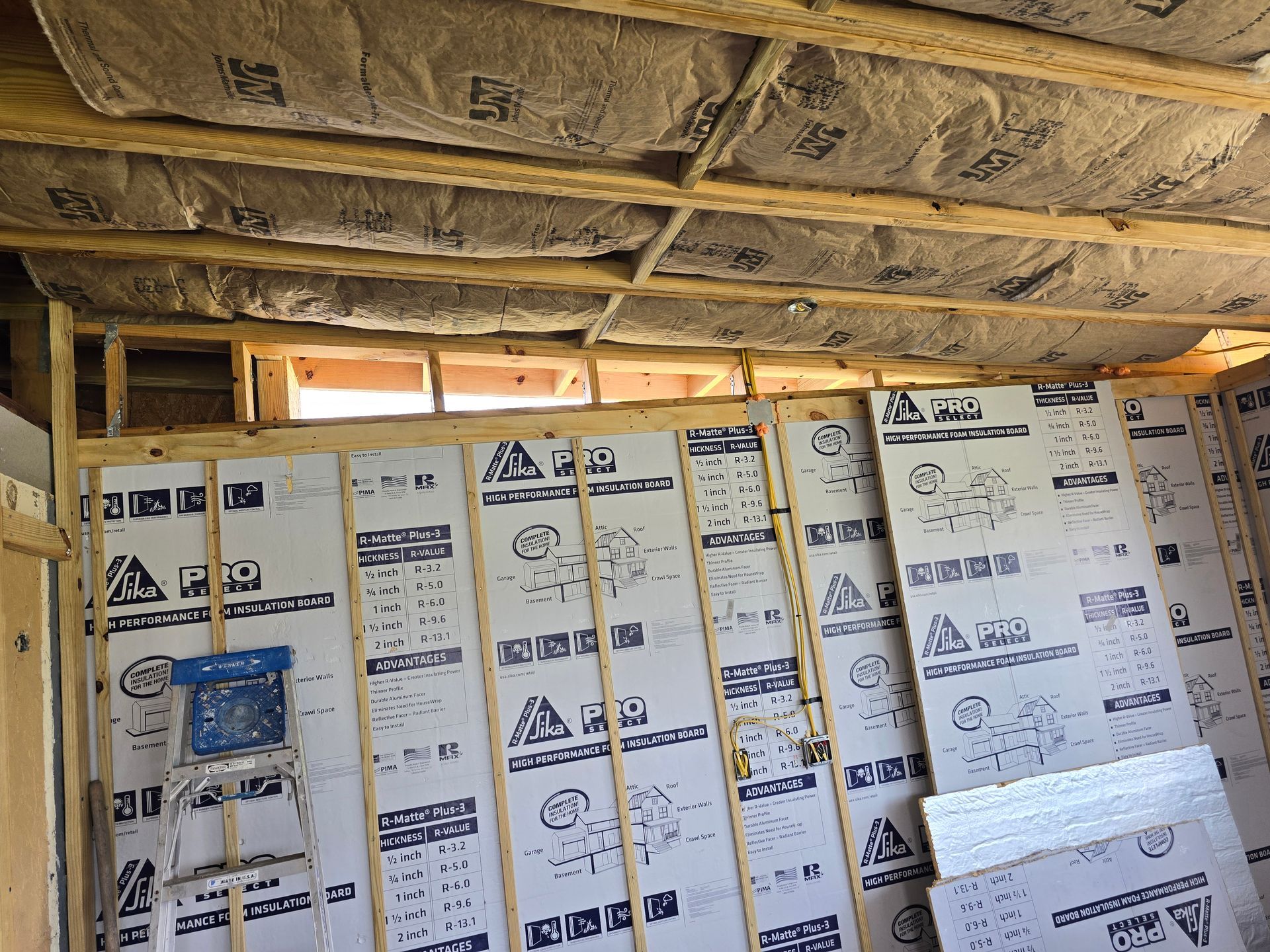 Insulated basement wall under construction with exposed ceiling joists and white foam board panels.