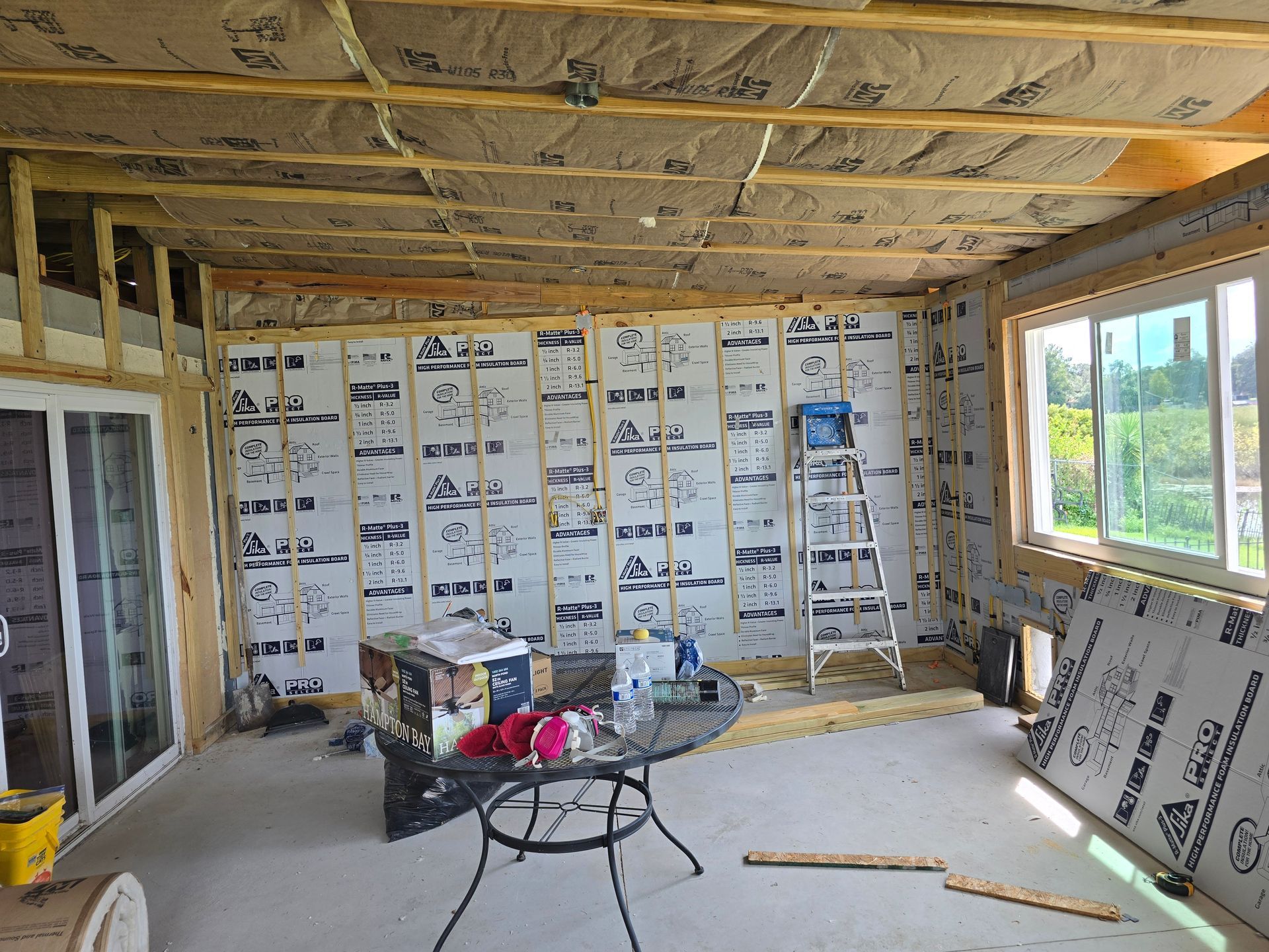 Unfinished room under construction with exposed insulation, tools on the floor, and a window on the right.