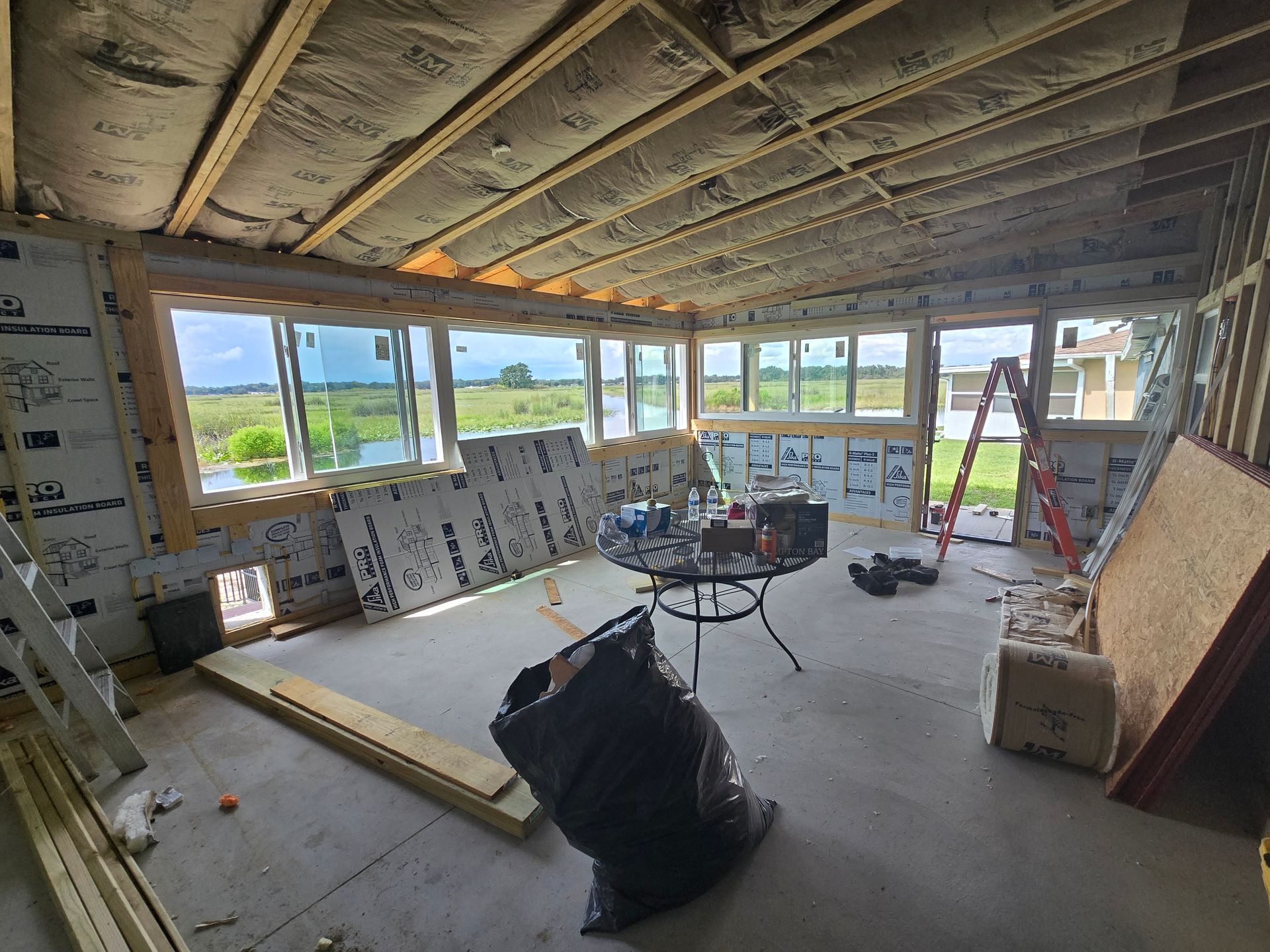 Partially renovated room with exposed ceiling, insulation, windows, tools, and construction materials