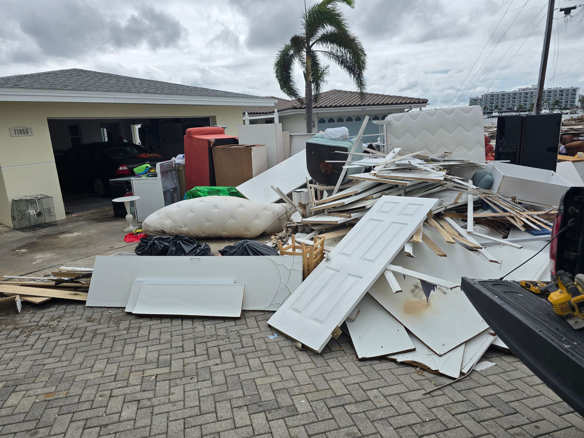 Storm debris piled in a driveway beside a damaged house and garage after severe weather.