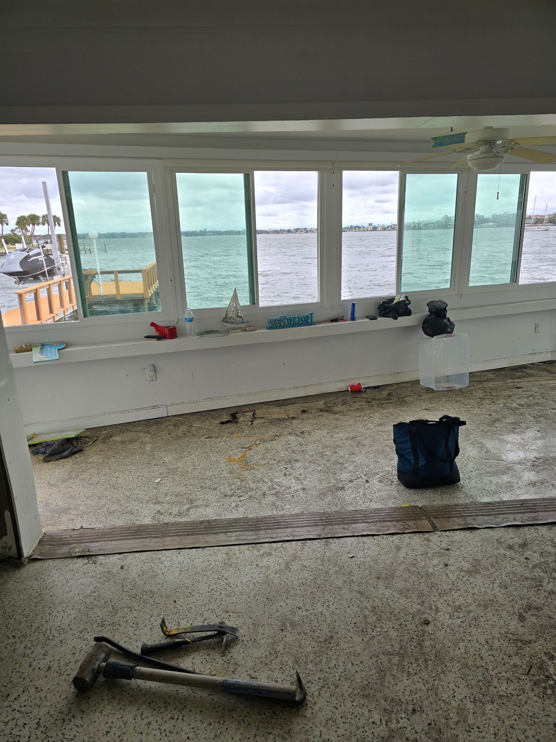 Debris-strewn room with broken windows and ocean view after storm damage