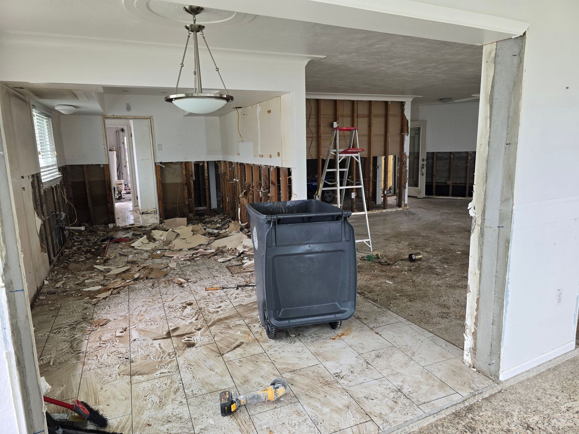 Damaged room under renovation, with exposed walls, debris, ladder, and a chair in the center.