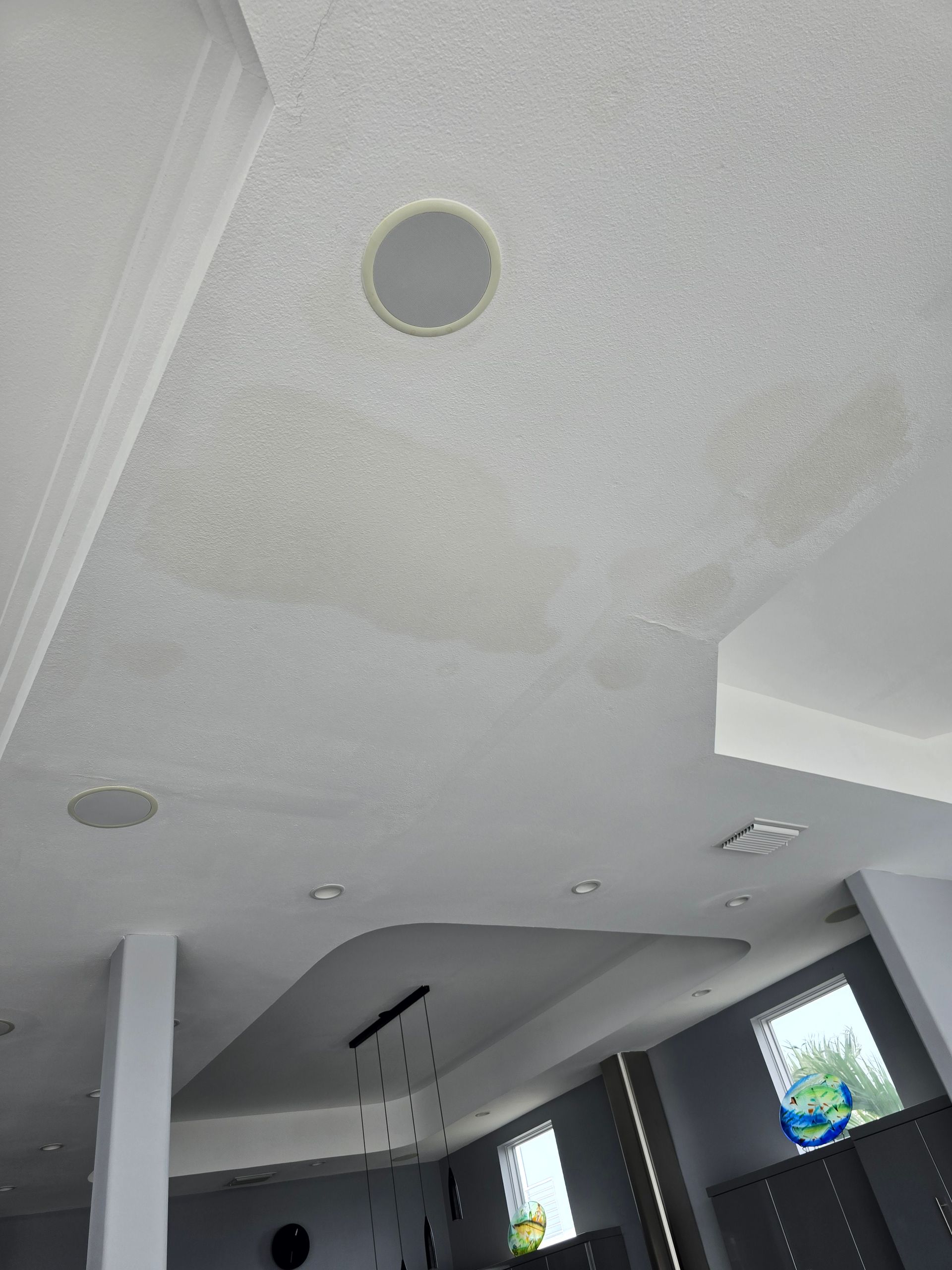 Modern interior room with white ceiling, recessed lights, and large windows showing blue sky.