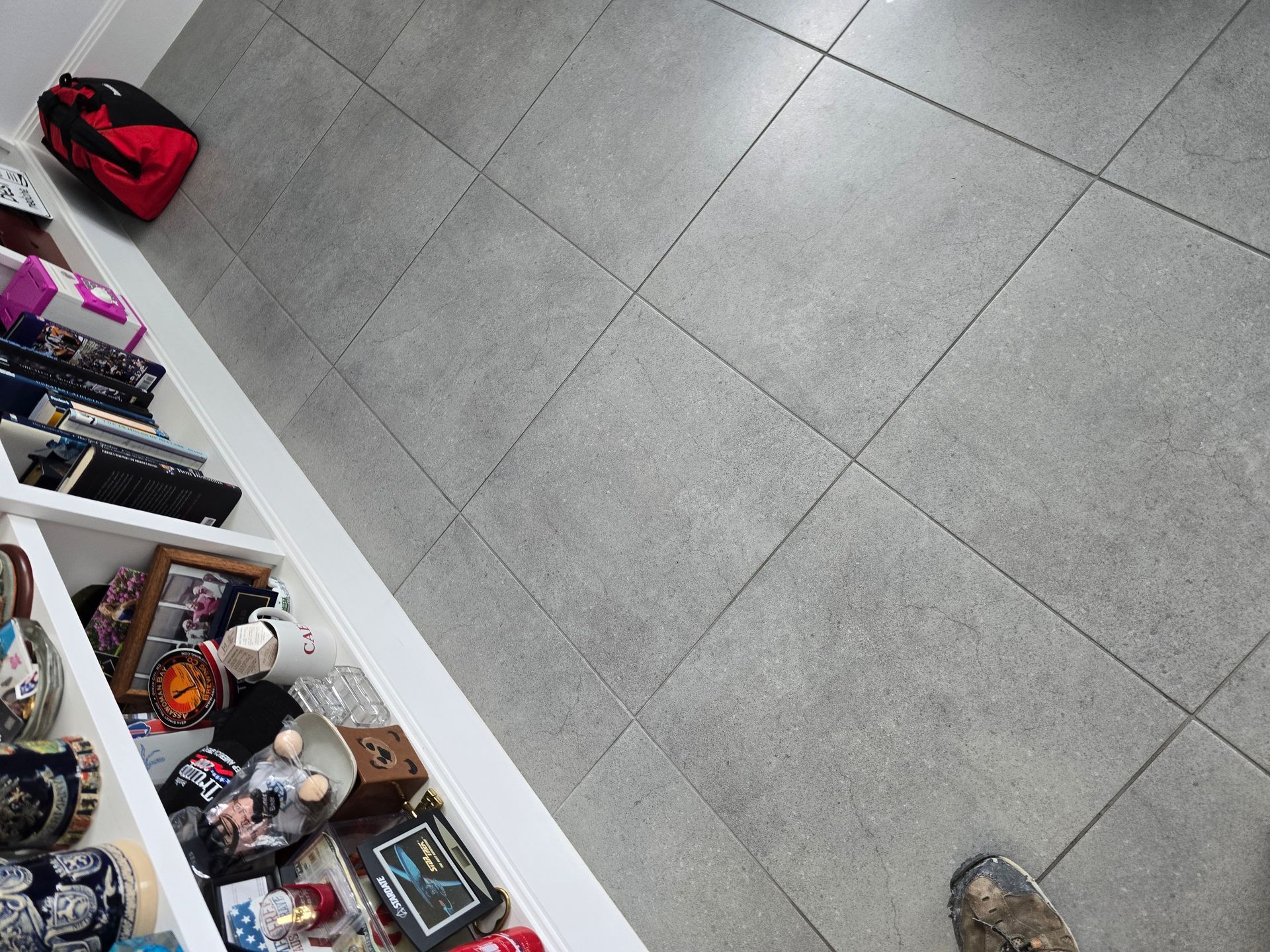 Gray tiled floor with a red bag near shelves of assorted items and a shoe at the bottom edge